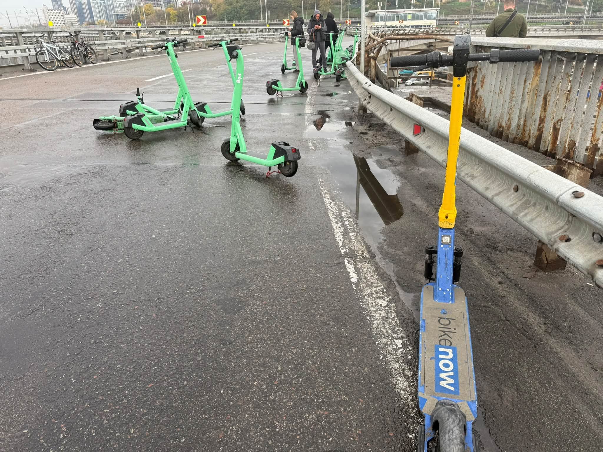 На мосту зі сторони метро Видубичі кияни залишили пару десятків самокатів компанії Bolt і один від Bike Now 